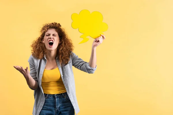 Mulher irritada gritando e segurando bolha de fala vazia em forma de nuvem, isolado em amarelo — Fotografia de Stock