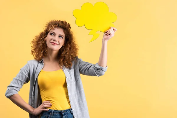 Mulher sorridente pensativo segurando bolha de fala vazia em forma de nuvem, isolado em amarelo — Fotografia de Stock