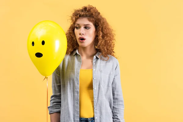 Тривожна дівчина тримає повітряну кулю з здивованим обличчям, ізольована на жовтому — стокове фото