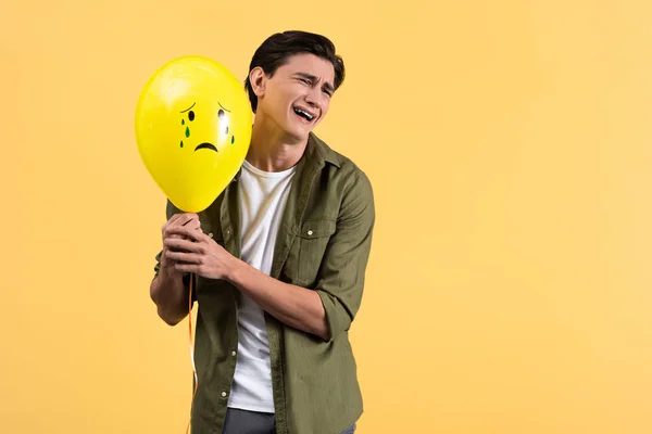 Sad crying young man holding balloon with tears, isolated on yellow — Stock Photo