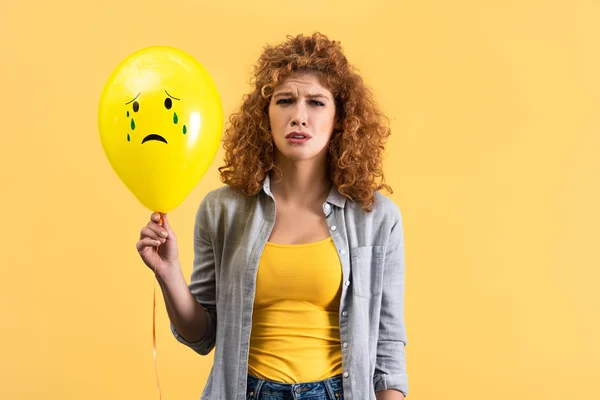 Chateado ruiva menina segurando triste balão com lágrimas, isolado no amarelo — Fotografia de Stock