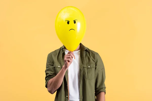 Junger Mann hält wütenden Luftballon vor Gesicht, isoliert auf gelb — Stockfoto