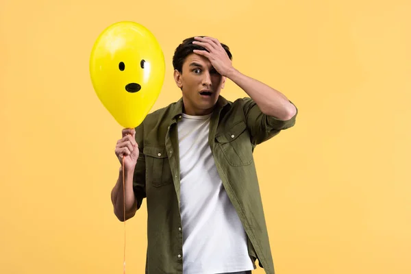 Preoccupato giovane uomo in possesso di palloncino scioccato, isolato su giallo — Foto stock