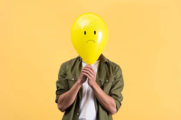 Jovem segurando balão triste na frente do rosto, isolado em amarelo — Fotografia de Stock