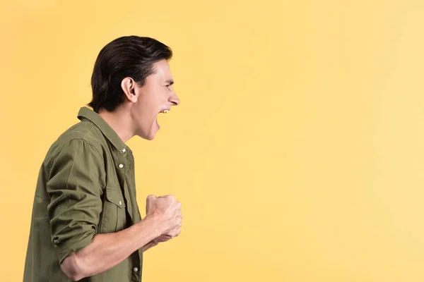 Angry young man yelling and holding fists, isolated on yellow — Stock Photo