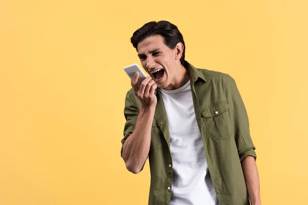 Joven enojado gritando en el teléfono inteligente, aislado en amarillo - foto de stock