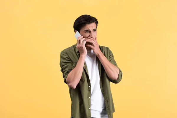 Розчарований молодий чоловік говорить на смартфоні, ізольований на жовтому — стокове фото