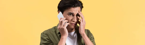 Панорамный снимок беспокойного молодого человека, разговаривающего на смартфоне, изолированного на желтом — стоковое фото