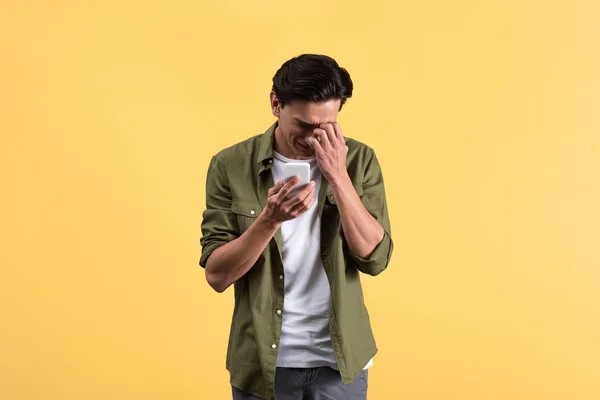 Emotional crying young man using smartphone, isolated on yellow — Stock Photo