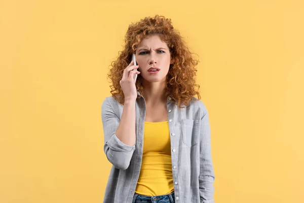 Рыжая женщина в плохом настроении говорит на смартфоне, изолирована на желтый — стоковое фото