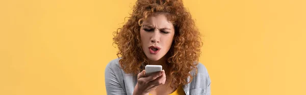 Panoramic shot of angry redhead woman yelling on smartphone, isolated on yellow — Stock Photo