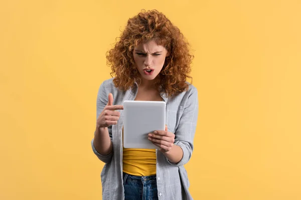 Menina agressiva apontando e gritando para tablet digital, isolado em amarelo — Fotografia de Stock