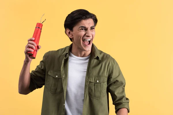 Сердитый молодой человек кричит и держит динамит палочки, изолированные на желтый — стоковое фото