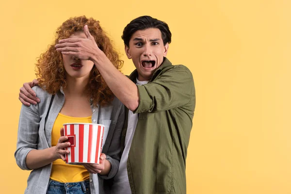 Homme effrayé crier et fermer les yeux à petite amie tout en regardant un film d'horreur, isolé sur jaune — Photo de stock