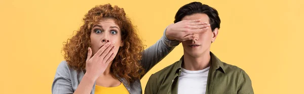 Panoramic shot of shocked scared girl closing mouth while closing eyes to boyfriend, isolated on yellow — Stock Photo
