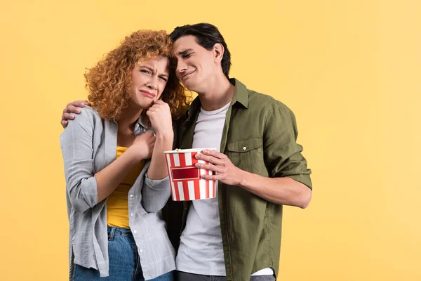 Couple bouleversé regarder film dramatique avec seau de maïs soufflé, isolé sur jaune — Photo de stock