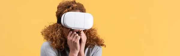 Panoramic shot of scared redhead woman using vr headset, isolated on yellow — Stock Photo