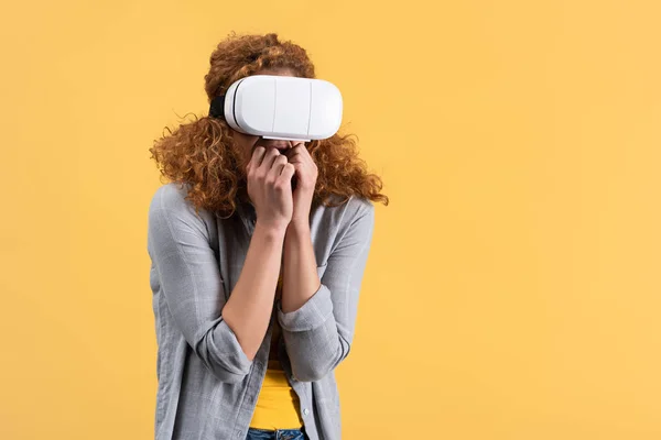 Chica pelirroja asustada usando auriculares de realidad virtual, aislado en amarillo - foto de stock