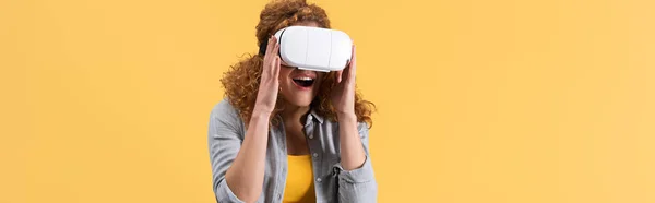 Panoramic shot of excited redhead woman using virtual reality headset, isolated on yellow — Stock Photo