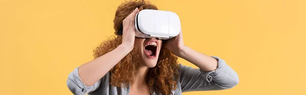 Panoramic shot of shouting emotional girl using virtual reality headset, isolated on yellow — Stock Photo