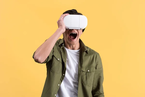 Joven emocionado gritando mientras usa auriculares de realidad virtual, aislado en amarillo - foto de stock
