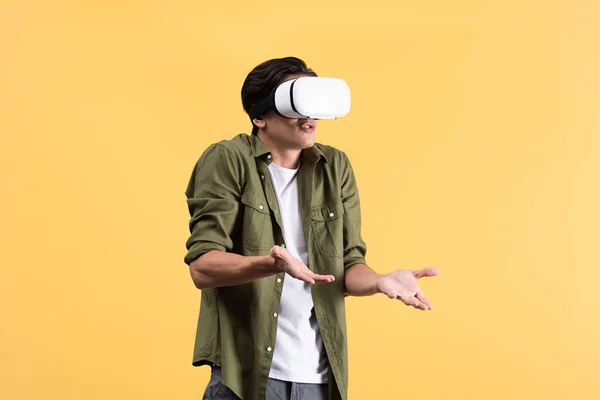 Раздраженный молодой человек с жест пожатия плечами с помощью VR гарнитуры, изолированные на желтый — стоковое фото