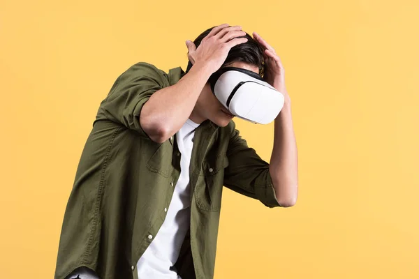 Переляканий молодий чоловік використовує гарнітуру віртуальної реальності, ізольований на жовтому — стокове фото