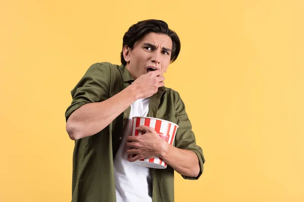 Jeune homme effrayé regardant un film d'horreur et mangeant du pop-corn, isolé sur jaune — Photo de stock