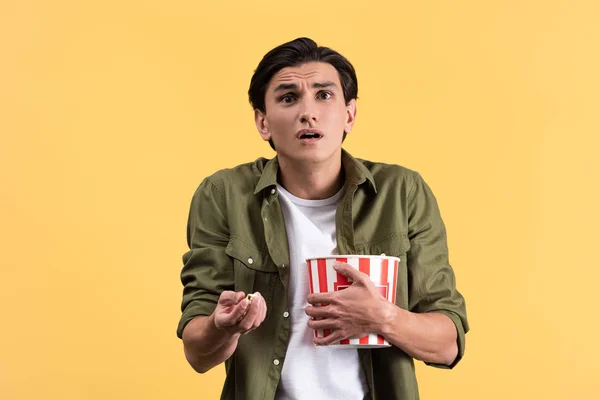 Scioccato giovane uomo guardando film con secchio di popcorn, isolato su giallo — Foto stock