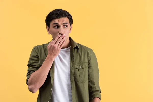 Shocked man in casual clothes closing mouth, isolated on yellow — Stock Photo