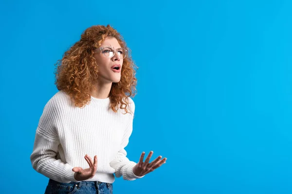 Aggressive yelling redhead girl in eyeglasses, isolated on blue — Stock Photo