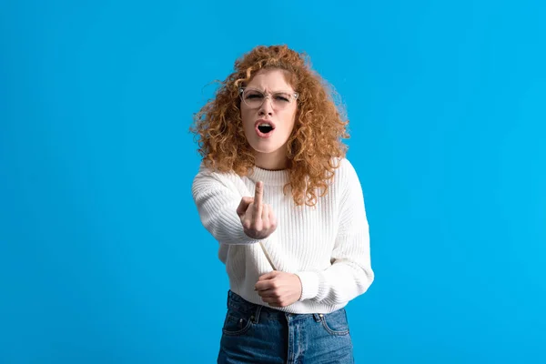 Mujer gritando estresada en gafas que muestran el dedo medio, aislado en azul - foto de stock