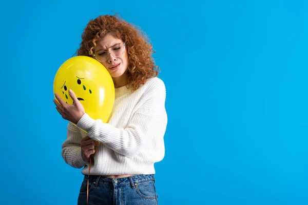 Chica pelirroja triste sosteniendo globo amarillo con la cara llorando, aislado en azul - foto de stock