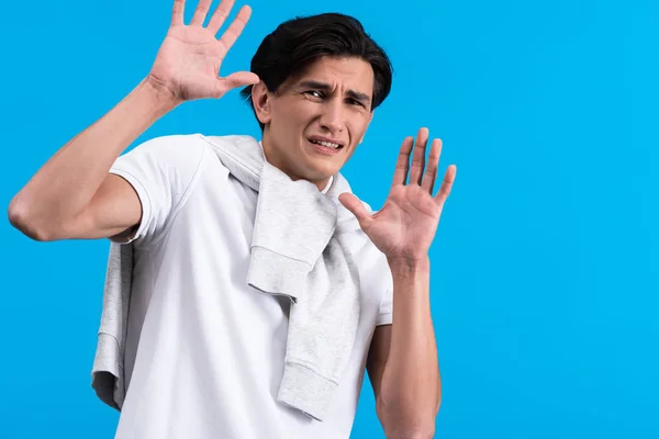Portrait of frightened young man with hands up, isolated on blue — Stock Photo