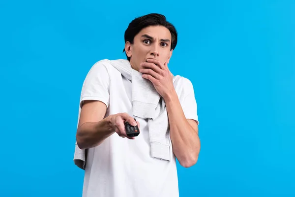 Shocked man watching tv with remote controller, isolated on blue — Stock Photo