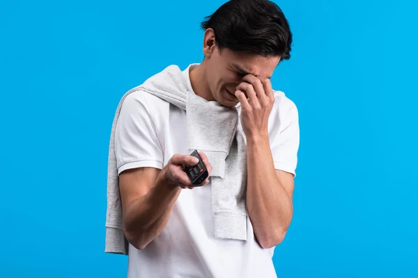 Trauriger Mann weint beim Fernsehen mit Fernbedienung, isoliert auf blauem Grund — Stockfoto