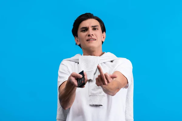 Aggressiver Mann zeigt Mittelfinger beim Fernsehen mit Fernbedienung, isoliert auf blauem Grund — Stockfoto