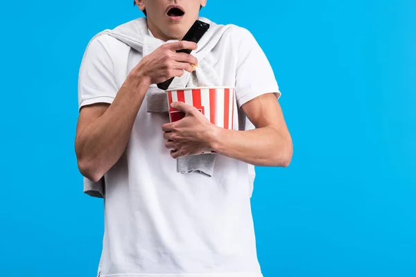 Vista ritagliata di uomo scioccato guardando la tv con telecomando e popcorn, isolato su blu — Foto stock