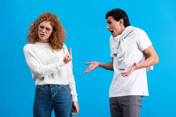 Irritated girlfriend showing middle finger to angry boyfriend, isolated on blue — Stock Photo