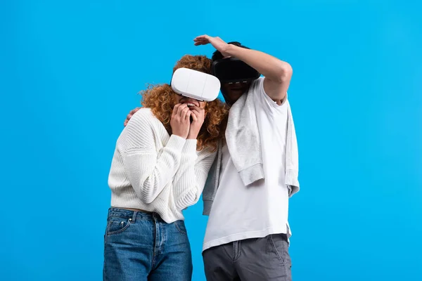 Couple effrayé à l'aide de casques de réalité virtuelle, isolé sur bleu — Photo de stock