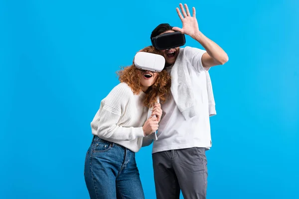 Aufgeregtes Paar mit Virtual-Reality-Headsets, isoliert auf blauem Grund — Stockfoto