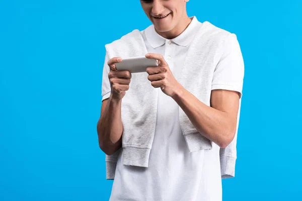 Ausgeschnittene Ansicht eines fokussierten jungen Mannes mit Smartphone, isoliert auf blau — Stockfoto
