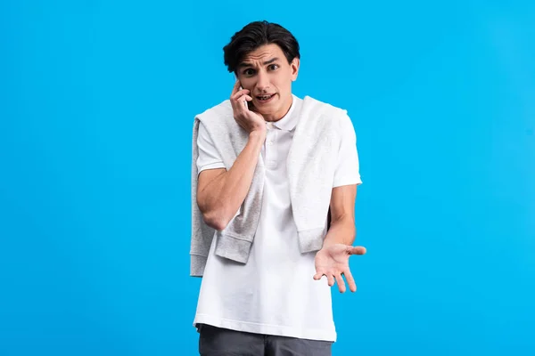 Irritated young man talking on smartphone, isolated on blue — Stock Photo