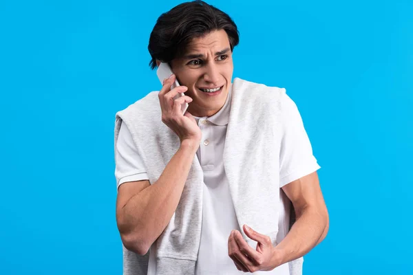 Angry young man talking on smartphone, isolated on blue — Stock Photo