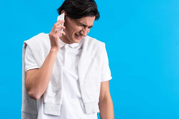 Stressed young man talking on smartphone, isolated on blue — Stock Photo