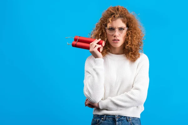 Confused woman in eyeglasses holding dynamite, isolated on blue — Stock Photo