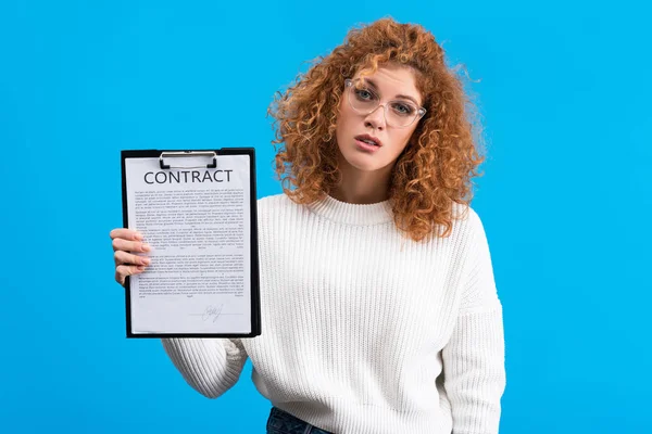 Приваблива скептична дівчина тримає буфер обміну з контрактом, ізольована на синьому — стокове фото