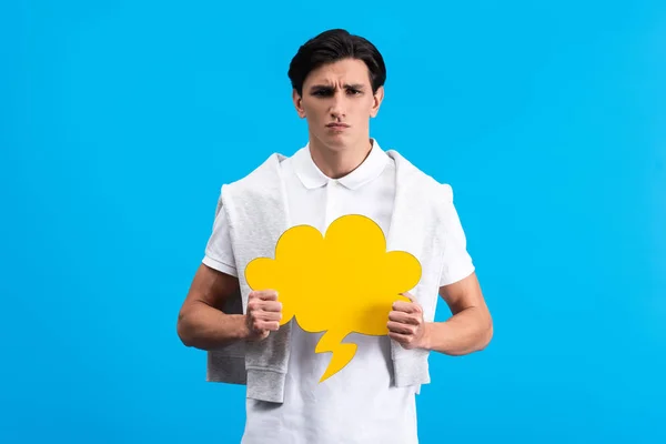 Irritated man holding yellow cloud speech bubble, isolated on blue — Stock Photo