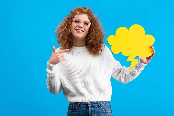 Mujer feliz apuntando a la burbuja del habla vacía en forma de nube, aislado en azul - foto de stock