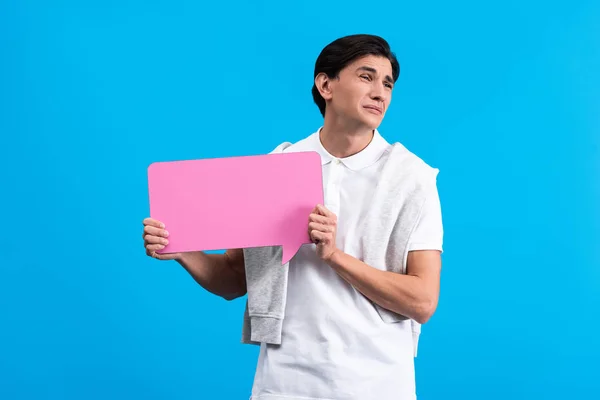 Hombre triste sosteniendo burbuja de habla rosa, aislado en azul - foto de stock